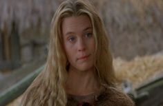 a woman with long blonde hair standing in front of hay bales and looking at the camera