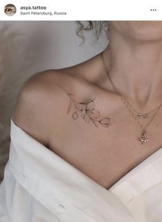 a woman with a tattoo on her chest is wearing a white dress and holding a necklace