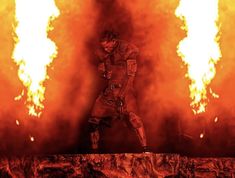 a man standing on top of a wooden platform in front of fire and flames behind him