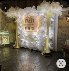 a party backdrop with white flowers and gold poles in front of a brick wall that reads, the little party never looked so nobody