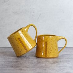 two yellow mugs sitting on top of a wooden table