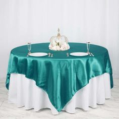 the table is set with two white plates on it and a green satin tablecloth