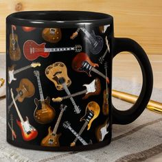 a black coffee mug with guitars on it sitting on a table next to a pen