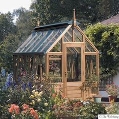 a small wooden greenhouse surrounded by plants and flowers