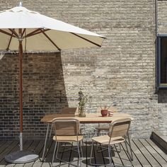 an outdoor table and chairs on a wooden deck next to a brick wall with windows