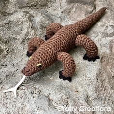 a crocheted lizard laying on top of a rock with scissors in it's mouth