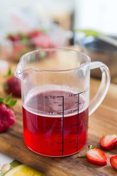 a pitcher filled with liquid sitting on top of a cutting board next to sliced strawberries