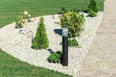 a black pole in the middle of a graveled area with trees and bushes around it