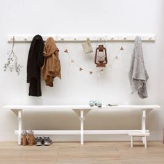 a white bench sitting next to a wall with clothes hanging from it's hooks