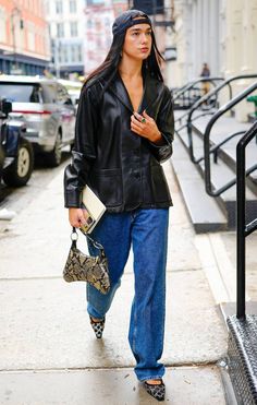 a woman is walking down the sidewalk with her handbag in her other hand and looking off into the distance