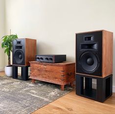 two speakers and a table with a plant on it in front of a white wall