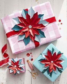 three wrapped presents with poinsettis on them sitting on a white wooden surface