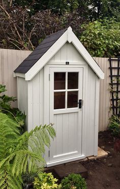 a small white shed sitting in the middle of a garden with lots of plants around it