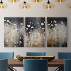 a dining room table with blue chairs and paintings on the wall above it that have flowers painted on them