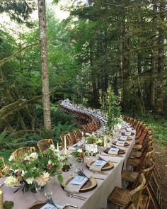 a long table is set up in the woods with place settings and flowers on it