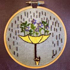 a hand embroidered picture of a yellow umbrella with purple flowers in the center and green leaves on it