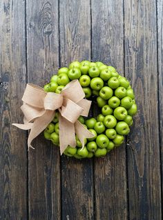 a wreath made out of green apples on top of a wooden table with a bow