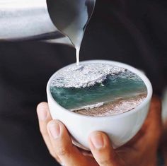 someone is pouring something into a cup with the ocean in it and waves coming out