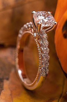 a close up view of a diamond ring on a wooden surface with an orange pumpkin in the background