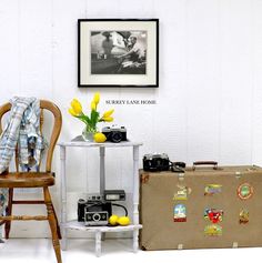 a chair, table and suitcase are sitting in front of a wall with pictures on it