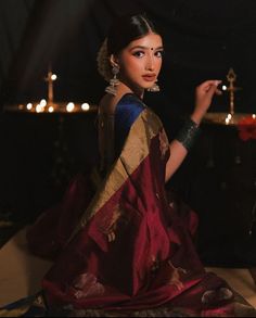 a woman in a red and gold sari sitting on the ground with candles behind her