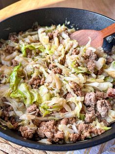 a skillet filled with meat and vegetables on top of a wooden table next to a blue towel