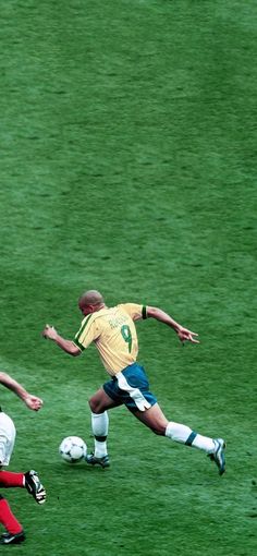 two men are playing soccer on a field with green grass and one is running after the ball