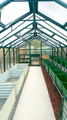 the inside of a greenhouse with several rows of green bins and gravel in them