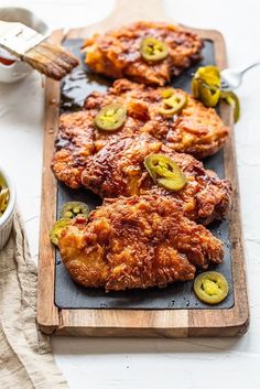 fried chicken with jalapenos and pickles on a cutting board next to a bowl of mustard