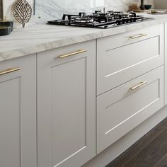 a white kitchen with marble counter tops and gold pulls on the cabinet doors is shown