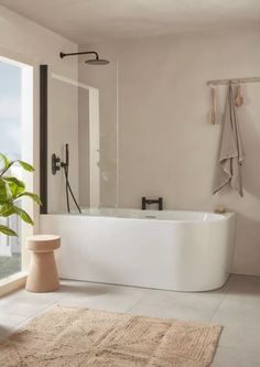 a large white bath tub sitting in a bathroom next to a window with a potted plant on it