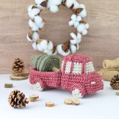 a crocheted red truck next to pine cones and cotton balls on a white surface