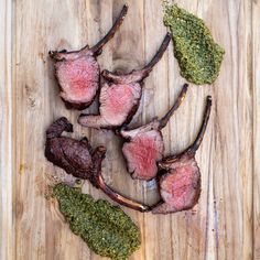 four pieces of steak on a wooden cutting board with herbs and seasoning next to it