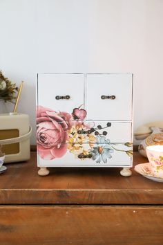 an old dresser with flowers painted on it and teacups in the foreground