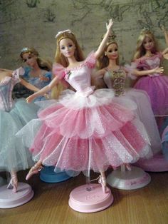 there are many barbie dolls that are on the table together and one is wearing a pink dress