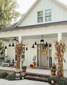 a white house with pumpkins and corn on the front porch for halloween decorating