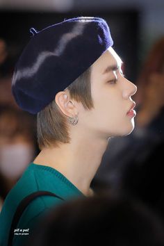 a young man wearing a blue beret and earring in front of a crowd