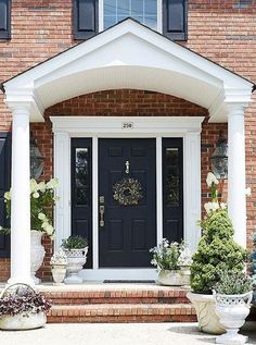 a black front door with white columns and potted plants