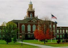 an old brick building with a flag on the roof and a clock tower in the background