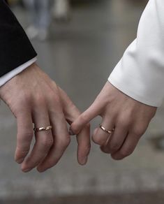 two people holding hands with gold wedding rings on their fingers and one wearing a black suit