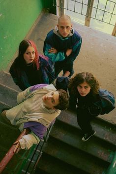 three young people sitting on the steps in front of a green wall, looking up at the camera