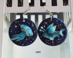 two earrings with fish on them hanging from hooks