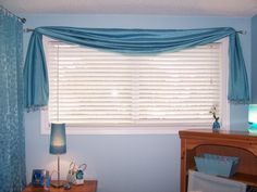 a bedroom with blue walls and curtains on the window sill, next to a night stand