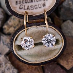 a pair of diamond earrings sitting in a box on top of some rocks and stones