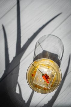 a glass filled with liquid sitting on top of a wooden table next to a shadow