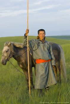 a man standing next to a brown horse in a green field with a stick on it's back