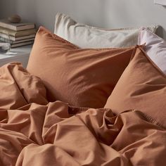 an unmade bed with two pillows and some books on the side table next to it