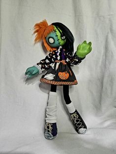 a doll with orange hair and green eyes is posed on a white sheeted background