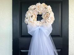 a wreath with white flowers hanging on the front door to someone's wedding party