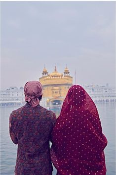 two women in red headscarves looking out over the water at a yellow building